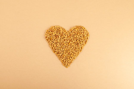Fenugreek Seeds (Methi Dana) in heart shape on beige background. Shambhala or helba seeds is traditional Indian seasoning and ingredient Ayurvedic food. Used in culinary and medicine.の写真素材