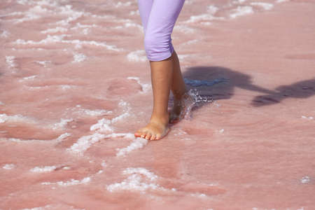 Treatment of flat feet. Children's feet walk on the surface of a pink lake with healing salt. Pink salt is used in alternative medicine.の写真素材
