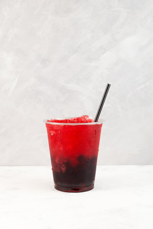 Fruit berries shaved ice in plastic cup. Slushie - drink on gray background. Refreshing summer drink...