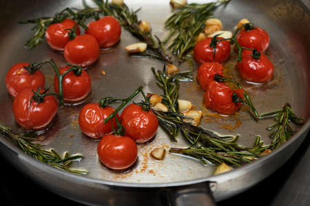 Cherry tomatoes fried in a frying pan with rosemary and garlic, close-up, selective focus.の写真素材
