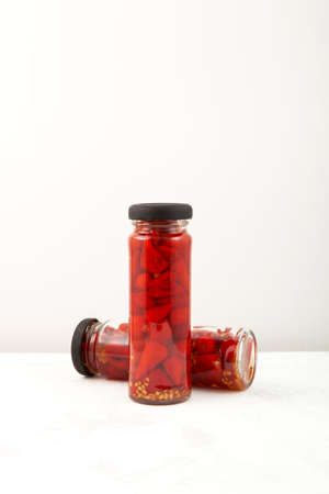 Red pickled mini chili peppers in glass jars. Preserved pepper, hot spice for meat or vegetarian...