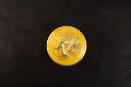 Glass of Yuzu iced drink on dark background, top view. Fruit citrus cocktail with ice cubes. Refreshing Iced drink. selective focus.の写真素材
