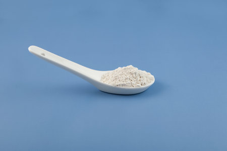 White chemical powder in ceramic spoon on blue. Food coloring, E171. Titanium dioxide, TiO2. Pigment...