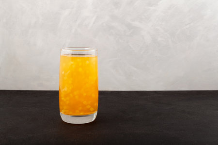 Refreshing tropical cocktail. Mango Yuzu Drink with Coconut jelly in tall glass on gray background. Fruit iced lemonade. Selective focus, copy space.の写真素材