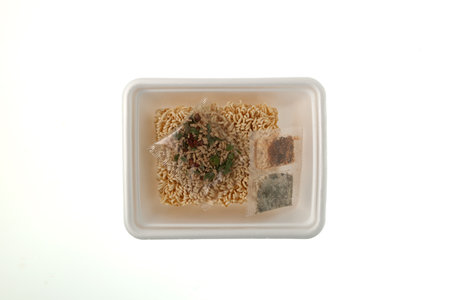 Dry pressed instant noodles with spicy in disposable tray on white background, top view. Fast food with food additives such as Monosodium glutamate, E627, E631 and other.の写真素材