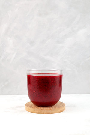 Red fruit berry smoothie in clear glass on gray background. Refreshing healthy cocktail, antioxidant slush drink.の写真素材