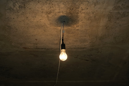 Dim light bulb on gray concrete ceiling of basement or bomb shelter. electric lamp. Temporary lighting from a mobile generator.の写真素材