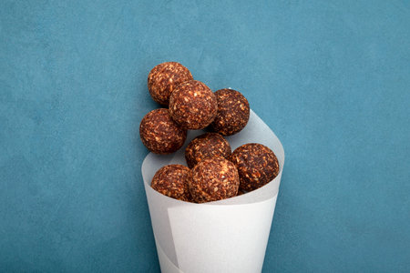 Energy balls with dried date fruits and carob powder. Vegetarian round candies in paper packaging on...