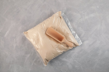 Transparent plastic bag of Soy Protein isolate and wooden scoop on gray background. Pure powder isolated from soybean is often used to increase the efficiency of fat burning.の写真素材