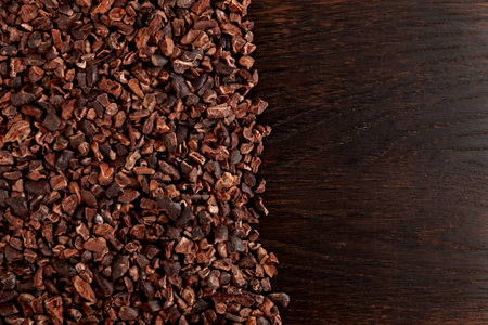 Cocoa nibs on brown wooden surface, close-up. Design element, copy space. Cocoa nibs are usually used to make a hot drink that tastes like hot chocolate. Sugar-free product, Natural antidepressant.の写真素材