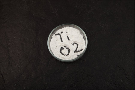 Titanium dioxide powder, TiO2 in Petri dish on dark stone table, top view. Food coloring, E171. Pigment has a wide range of applications, including paint, food, toothpastes, and cosmetic products.の写真素材