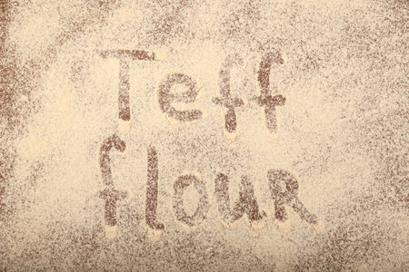 Organic Teff Flour scattered on brown surface with inscription Teff flour. trendy superfood. design element.の写真素材