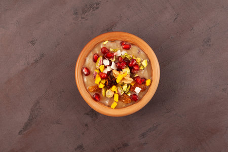Noah's pudding or Noah's Dessert. Ashure or Asura Dessert, also called as Anusabur in clay bowl on brown background, top view. Turkish delicious porridge with grains, fruits, and nuts.の写真素材