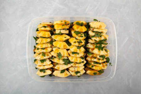 Fermented Pineapple slices with mint leaf in cane sugar syrup. Traditional Asian fruit salad in plastic container on gray background, top view. Sweet Pineapple dessert.の写真素材
