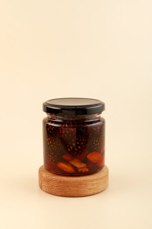 Jam with pine cones, almond nuts and walnuts in glass jar on beige background. Healthy sweet sugar syrup to support the immune system. alternative therapy.の写真素材