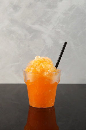 Disposable Plastic Cup of Orange Granizado or Orange Slushie drink with natural juice. Fruit shaved ice. Refreshing summer drink on gray background.の写真素材