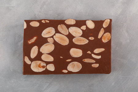 Chocolate Turron with almonds on gray textured background, top view. Traditional Spanish Turron with cocoa, milk chocolate and nuts.の写真素材