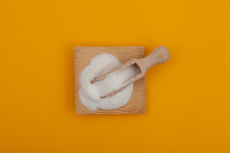Food additive E316 in measuring scoop on yellow background. Sodium erythorbate, Sodium D-isoascorbate or araboascorbic acid. Chemical formula C6H7NaO6. White crystalline powder.の写真素材