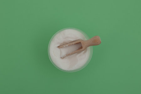 Food additive E316 in plastic bowl with wooden measuring scoop, top view. Sodium erythorbate or sodium isoascorbate used in meats, poultry, soft drinks. White powder with chemical formula C6H7NaO6.の写真素材