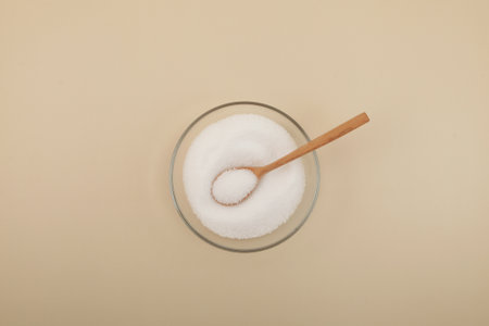 Sugar substitute in glass plate with spoon, top view. Artificial sweetener. White crystalline powder.の写真素材