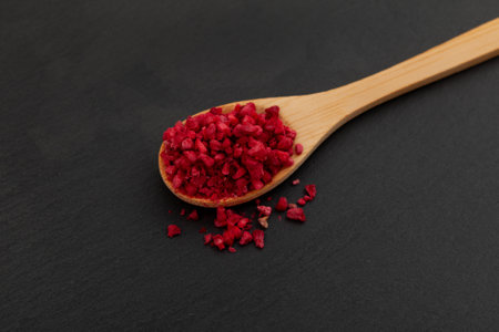 Crunchy pieces of Freeze dried raspberries in wooden spoon, close-up. Selective focus. Dehydrated raspberry berries. Delicious fruit topping for porridge, cereal, yogurt and desserts.の写真素材