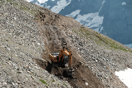 Excavator working behind on the slope in mountainous terrain. Heavy excavator is building a road through a mountain pass.の写真素材