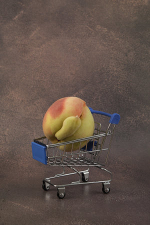 Peach in shopping trolley on brown textured background. Selective focus, copy space. Concept - Food waste reduction. Using imperfect products.の写真素材