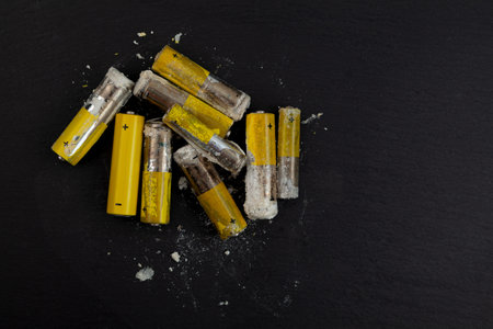 Oxidized and leaked AA alkaline batteries on dark surface. White powder was formed by leakage of alkaline electrolyte.の写真素材