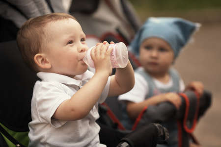 cute baby drinks juice sitting in baby carriageの写真素材