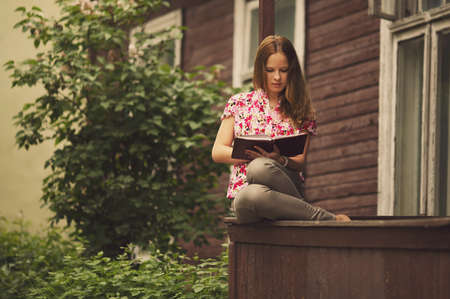 beautiful girl reading book sitting on the porch of  houseの写真素材