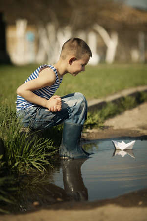 little happy boy plays with paper boats in puddleの写真素材