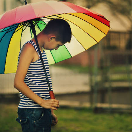 sad boy with colorful rainbow umbrellaの写真素材