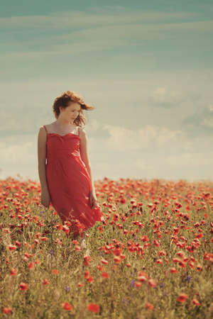young red haired beautiful girl in poppy fieldの写真素材