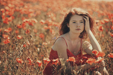 young red haired beautiful girl in poppy fieldの写真素材