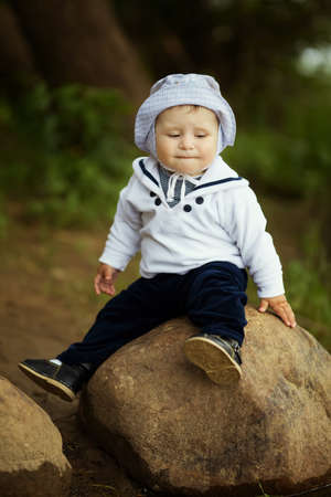 little boy sitting on big stone near lakeの写真素材