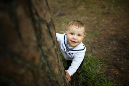 cute beautiful baby hiding behind tree in parkの写真素材