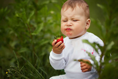 little funny boy sitting in grass with strawberryの写真素材