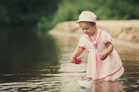 little girl plays with paper boats in riverの写真素材