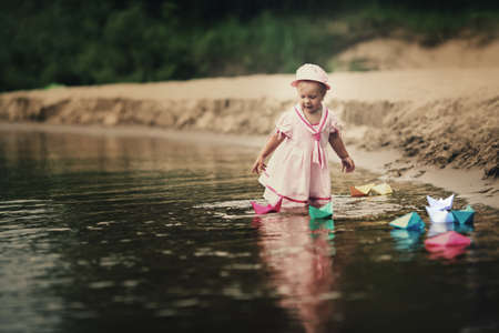 little girl plays with paper boats in riverの写真素材