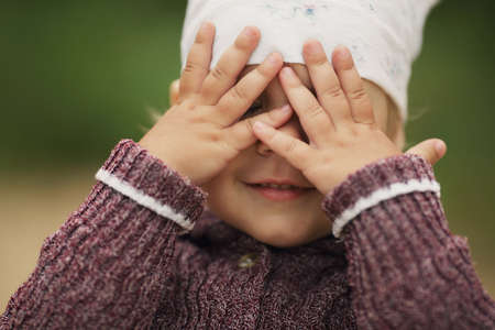little girl is playing hide-and-seek hiding faceの写真素材