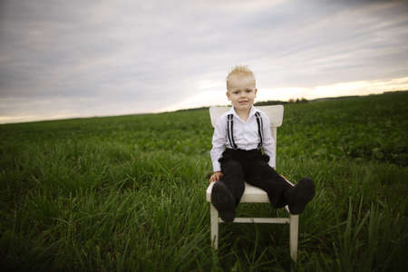 little boy sits on chair in the fieldの写真素材