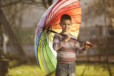 little happy boy with a rainbow umbrella in parkの写真素材
