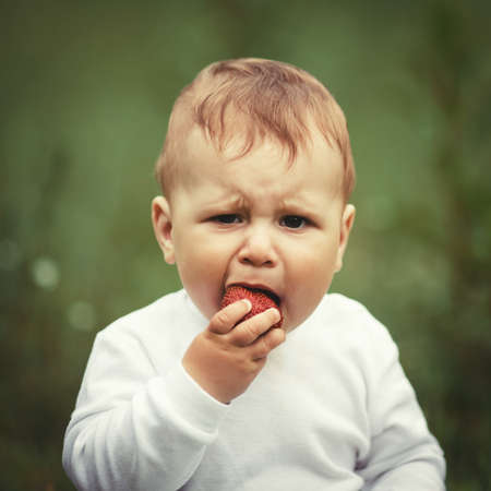 little funny boy sitting in grass with strawberryの写真素材