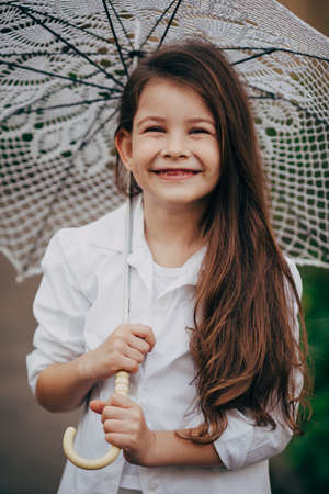 small and pretty  smiling girl with lace umbrella in white suitの写真素材