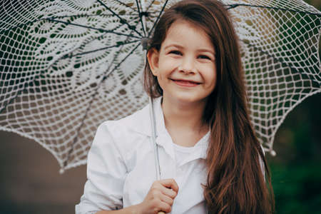 small and pretty  smiling girl with lace umbrella in white suitの写真素材