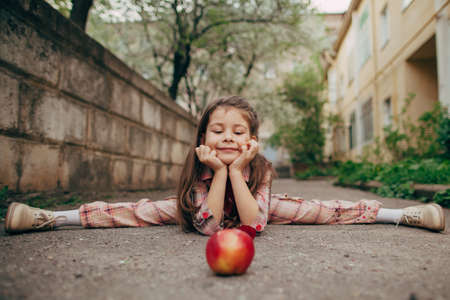 small pretty girl doing splits and looking for red appleの写真素材