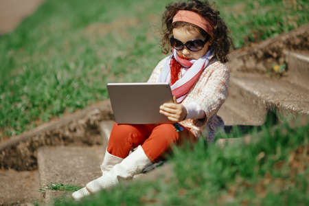 little and pretty girl sitting on the stairs of stone and working as businesswoman
