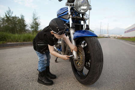 cute little biker repairs motorcycle on road