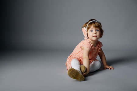 cute little girl sitting on grey background