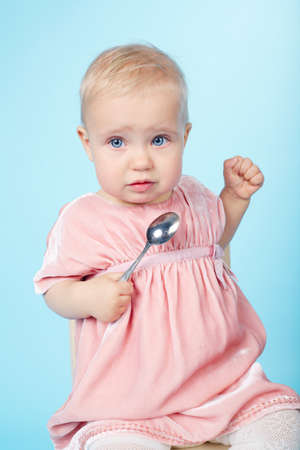 cute little girl with spoon sitting on chairの写真素材